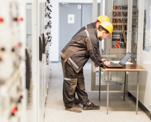 Two maintenance engineers inspect relay protection system with laptop