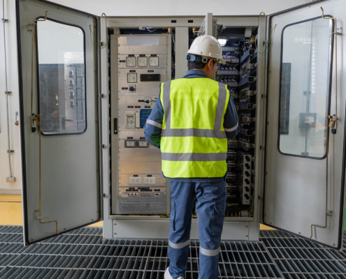 Electrical technician inspecting wiring and components inside open control cabinet